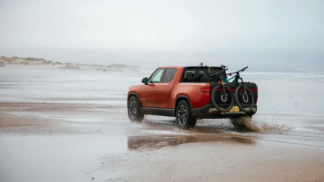 Red Rivian R1T pickup carrying bicycles beside the ocean
