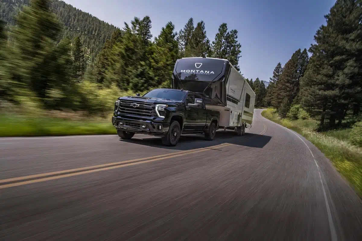 2027 Chevrolet Silverado HD High Country towing a fifth-wheel trailer on a mountain road