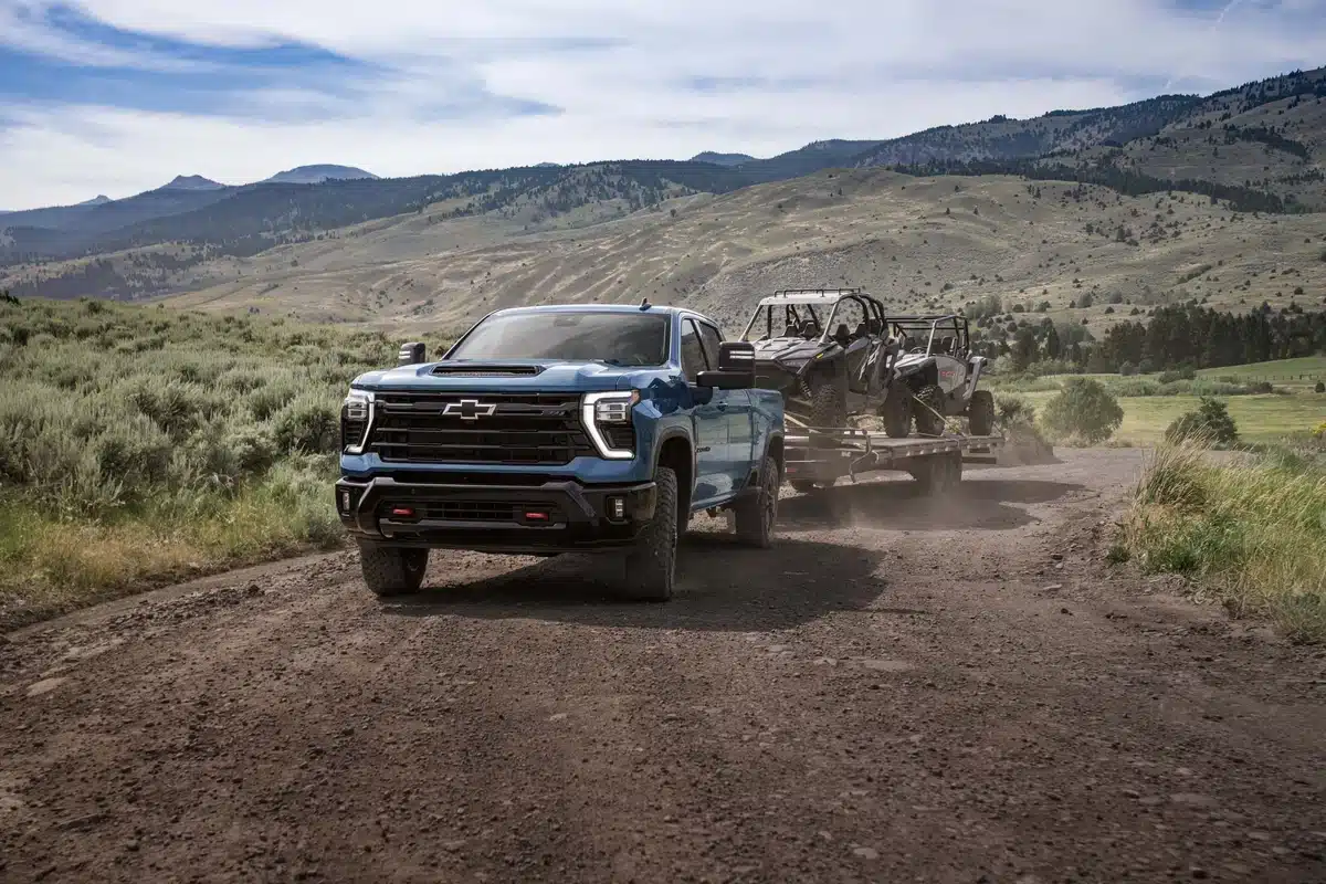 Blue 2027 Chevrolet Silverado HD Z71 towing two UTVs on a dirt road