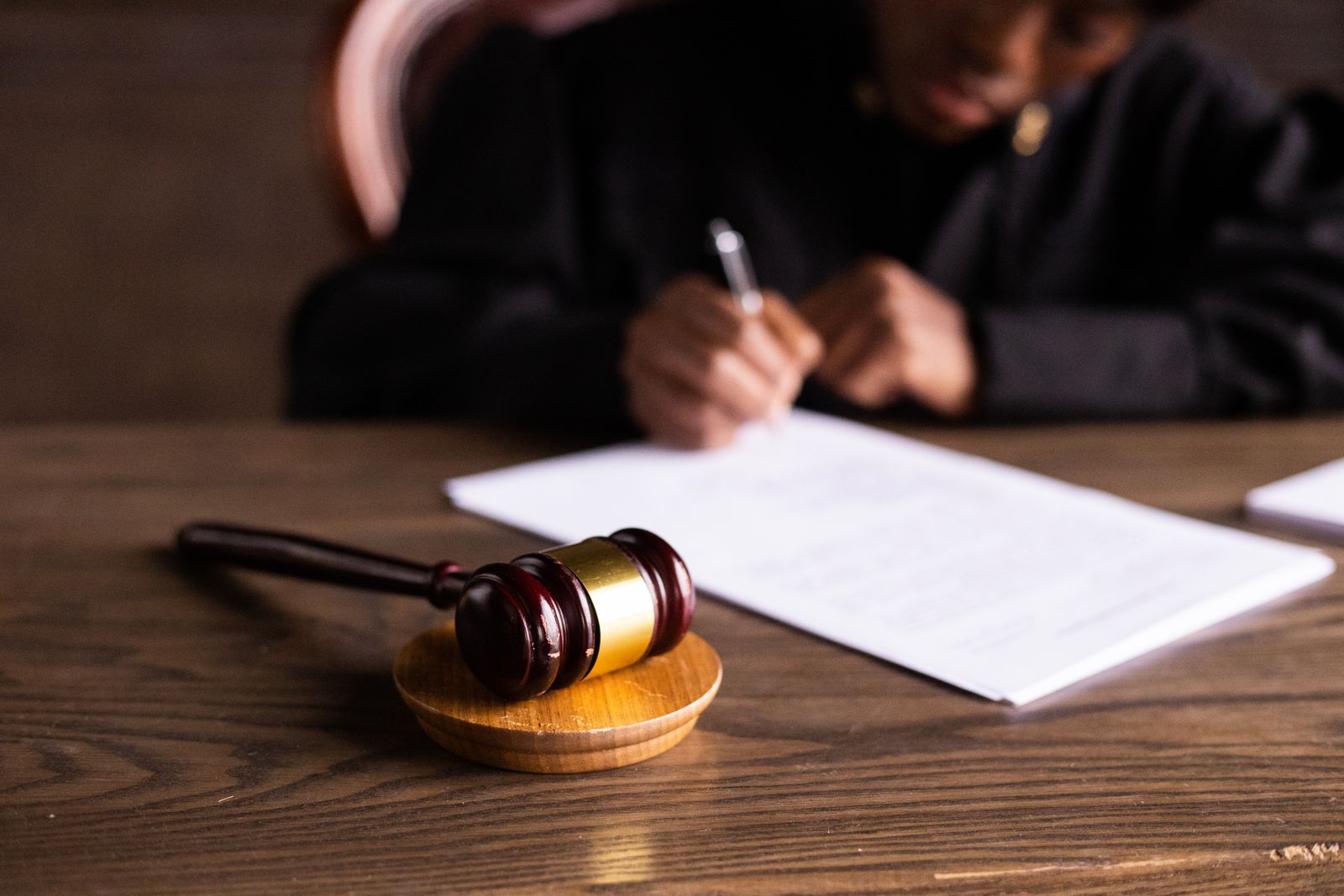 Stock photo of a judge writing on documents with a wooden gavel in the foreground.